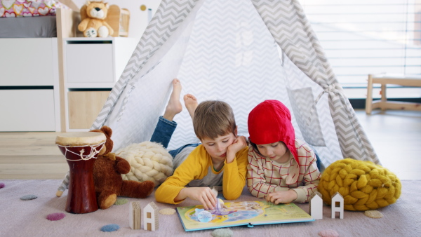 Small children in bedroom indoors at home, reading book in tent.