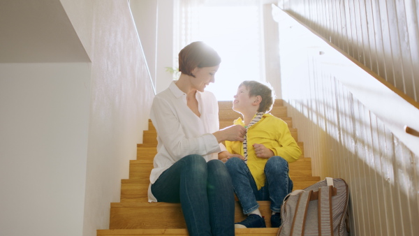 Mother with small son on staircase in the morning at home, getting ready for school.