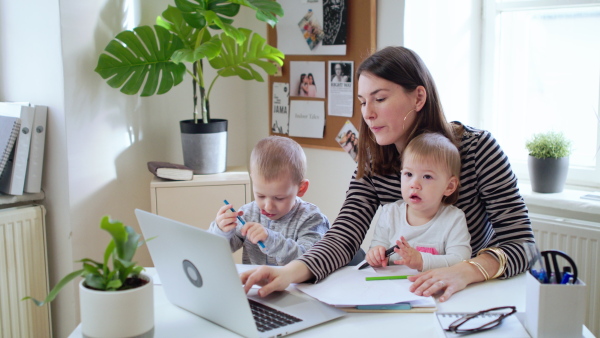 Mother with two small children and laptop working in home office, quarantine concept.