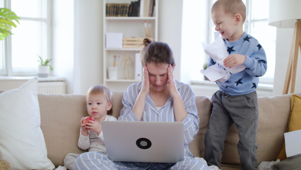 Stressed mother with small children wearing pajamas working in home office, quarantine concept.