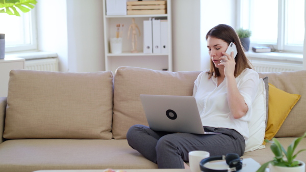 Young businesswoman with laptop and smartphone working on sofa in home office, quarantine concept.