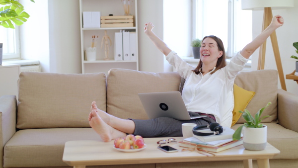 Businesswoman with laptop working in home office in quarantine, expressing excitement.