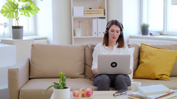 Young businesswoman with laptop and headphones working on sofa in home office, quarantine concept.