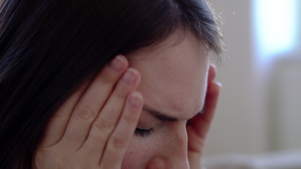 Close-up of sad and depressed woman holding head indoors, mental health concept.