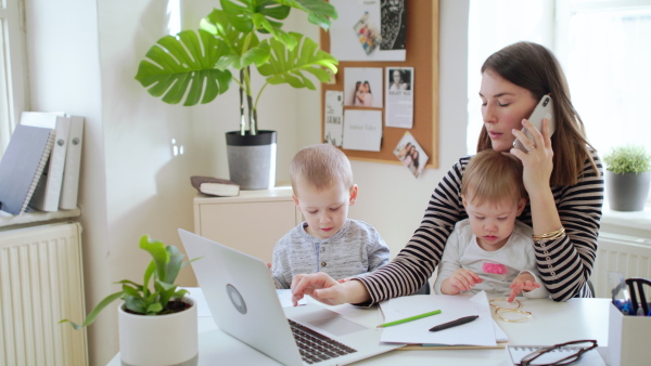 Mother with two small children and laptop working in home office, quarantine concept.