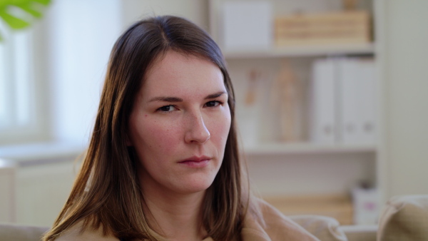 Close-up of sad and depressed woman looking at camera indoors, mental health concept.