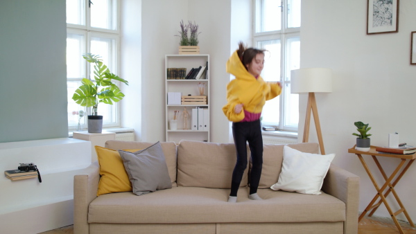 Front view of small girl jumping on sofa indoors at home, having fun.