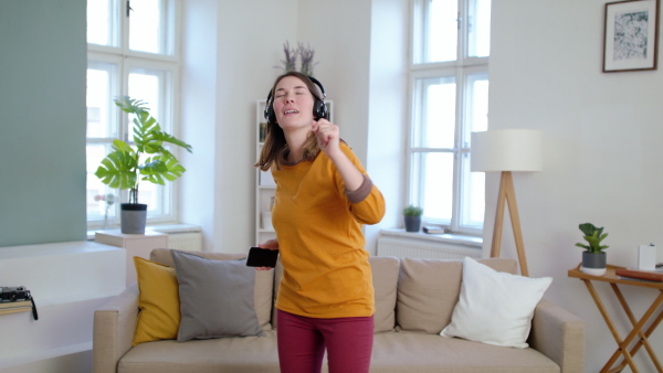 Young woman with headphones listening to music and dancing indoors at home, quarantine concept.