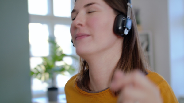 Close-up of young woman with headphones listening to music and dancing indoors at home, quarantine concept.