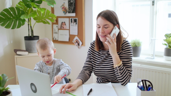 Mother with small son, laptop and smartphone working in home office, quarantine concept.