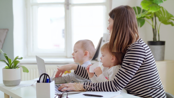 Mother with two small children and laptop working in home office, quarantine concept.