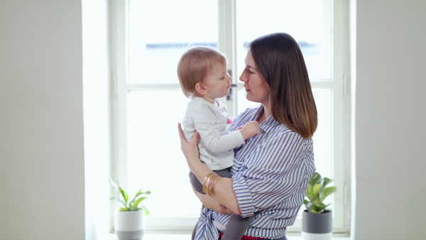 Happy working mother with small daughter kissing in home office, quarantine concept.