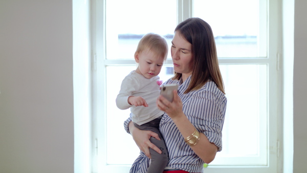 Mother with small daughter and smartphone working in home office, quarantine and lockdown concept.