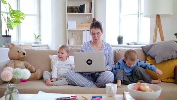 Mother and small children with pajamas, laptop and smartphone children working in home office, quarantine concept.