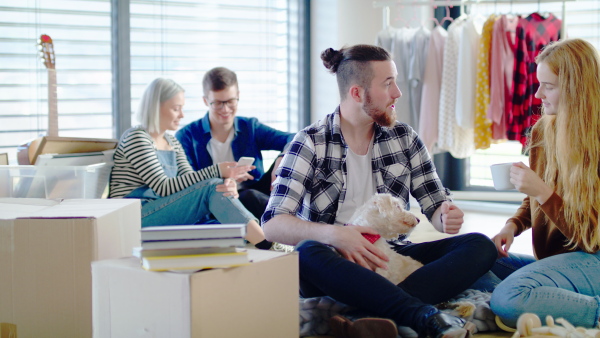 Group of cheerful young people with dog moving in new home, house sharing concept.