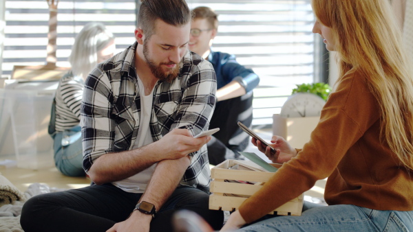 Group of cheerful young people with smartphone moving in new home, house sharing concept.