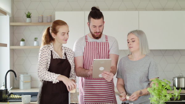 Group of young people with tablet cooking together at home, house sharing concept.