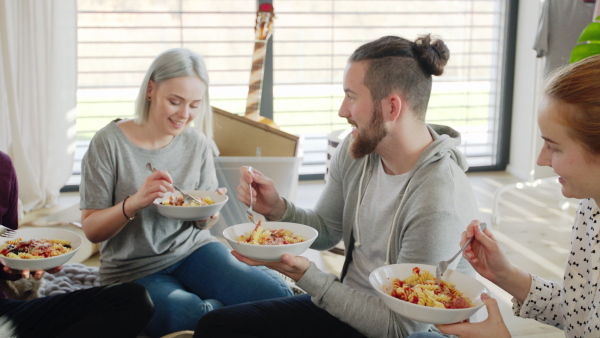 Group of young people with pet dog moving in new home, eating. House sharing concept.