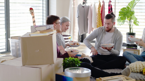 Group of young people with pet dog moving in new home, eating. House sharing concept.