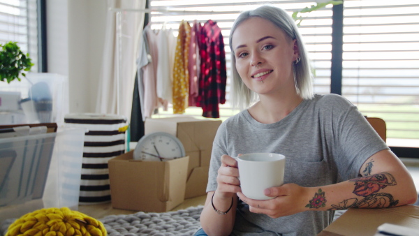 Portrait of young woman with coffee moving in new home, looking at camera.