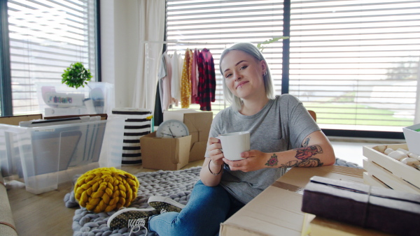 Portrait of young woman with coffee moving in new home, looking at camera.