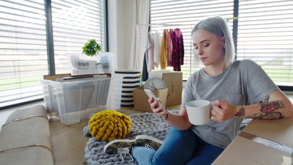 Portrait of young woman with smartphone and coffee moving in new home.