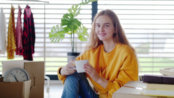 Portrait of young woman with coffee moving in new home, looking at camera.