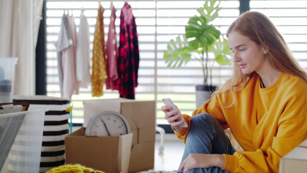 Portrait of young woman with smartphone and coffee moving in new home.