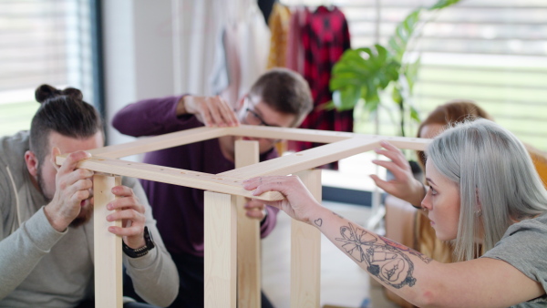 Group of young people assembling furniture in new home, house sharing concept.