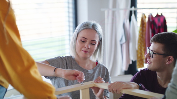 Group of young people assembling furniture in new home, house sharing concept.