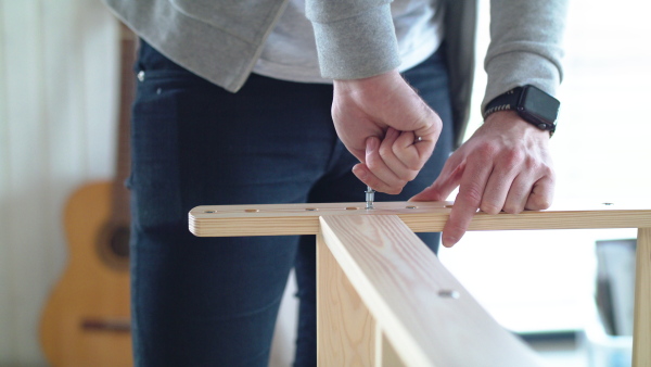 Midsection of unrecognizable young man assembling furniture in new home, house sharing concept.