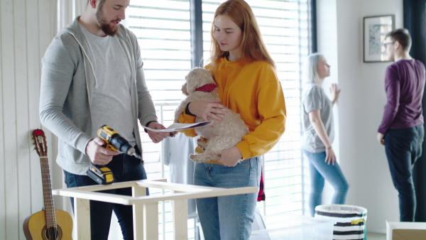 Group of young people with dog assembling furniture in new home, house sharing concept.