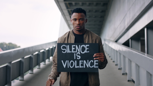 Young man with silence is violence sign standing outdoors in city, black lives matter concept.