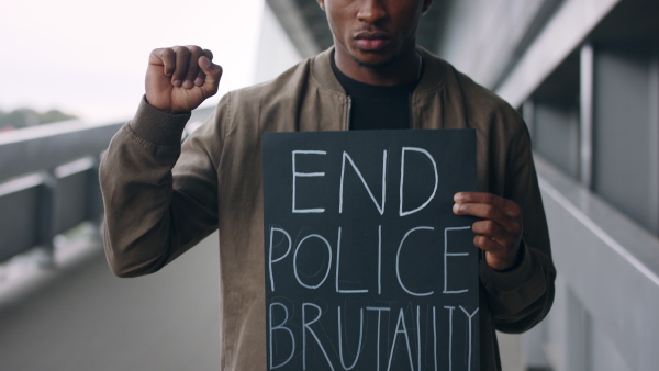 Young man with end police brutality sign standing outdoors in city, black lives matter concept.