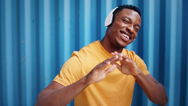 Young black man with sunglasses and headphones standing against blue background, black lives matter concept.