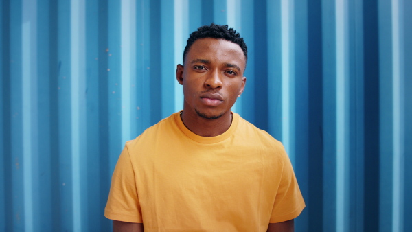 Young black man with raised in yellow shirt fist standing against blue background, black lives matter concept.