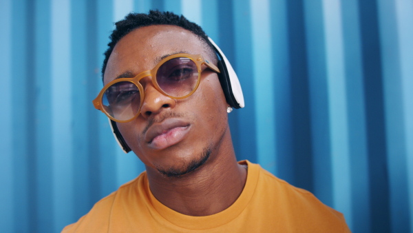 Young black man with sunglasses and headphones standing against blue background, black lives matter concept.