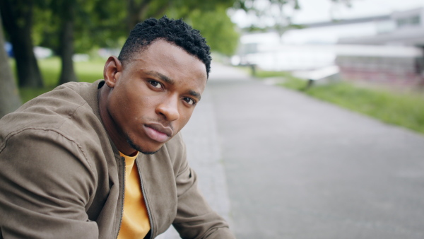 Young black man commuter sitting on bench outdoors in city, laughing.