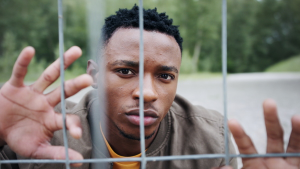 Frustrated young black man behind net outdoors in city, black lives matter and discrimination concept.