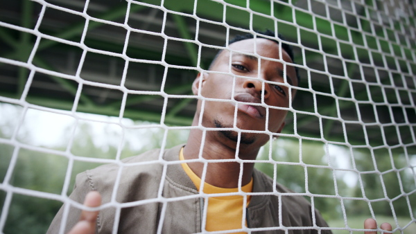 Frustrated young black man behind net outdoors in city, black lives matter and discrimination concept.