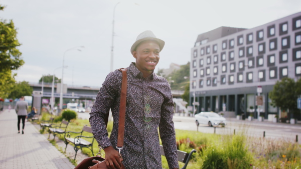 Cheerful young black man commuter walking outdoors in city, greeting somebody.