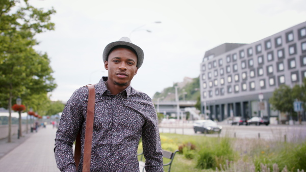 Young black man commuter with hat outdoors in city, walking.