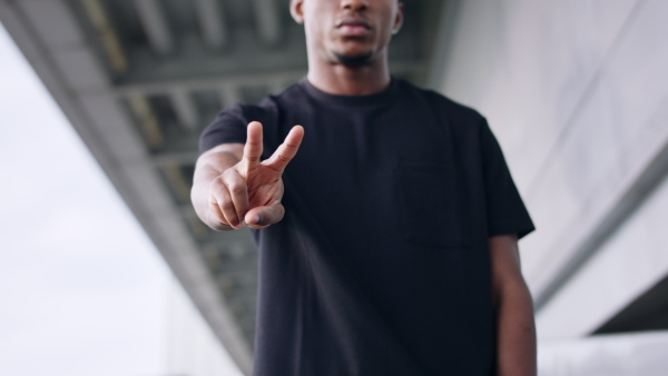 Portrait of black man with peace gesture outdoors in city, black lives matter concept. Close up on hand.