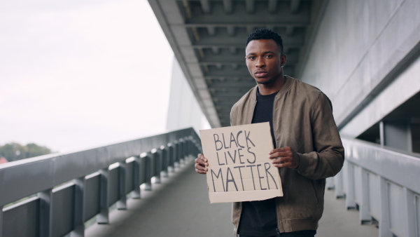 Young man with blac lives matter sign standing outdoors in city, black lives matter concept.