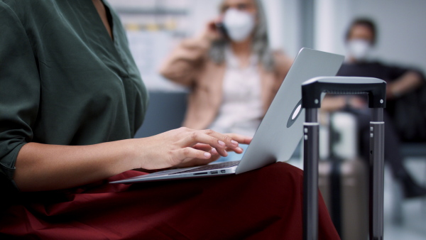 A group of passengers waiting for flight, close up on woman typing on laptop. Coronavirus concept.