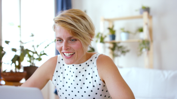 Portrait of cheerful young businesswoman with laptop indoors in home office, having video call.