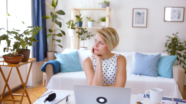 Front view of cheerful young businesswoman with laptop indoors in home office, resting when working.