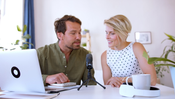 Front view of happy couple with microphone having video call on laptop indoors at home.