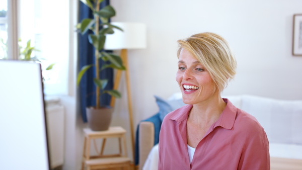 Portrait of cheerful young businesswoman with laptop indoors in home office, having video call.