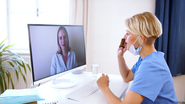 Side view of woman doctor having video call with patient on laptop, online consultation concept.